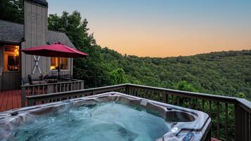 A hot tub on a deck with a view of a forested hillside.
