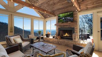 A spacious room with a stone fireplace, wicker furniture, and large windows offering a view of the mountains.
