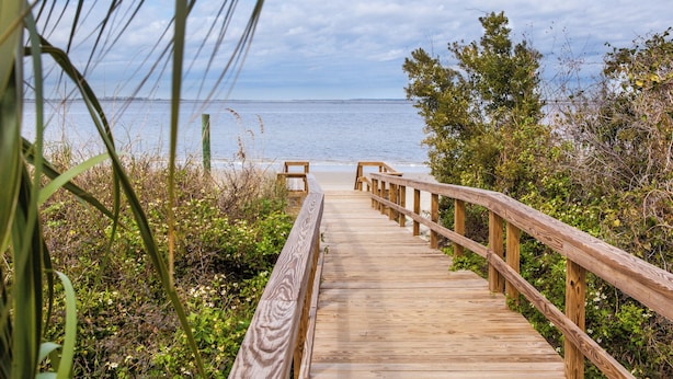 Une promenade en bois qui mène à une plage offrant une vue dégagée sur l’océan.