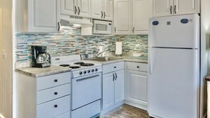Une cuisine avec des meubles blancs, une cuisinière, un four à micro-ondes et un réfrigérateur.