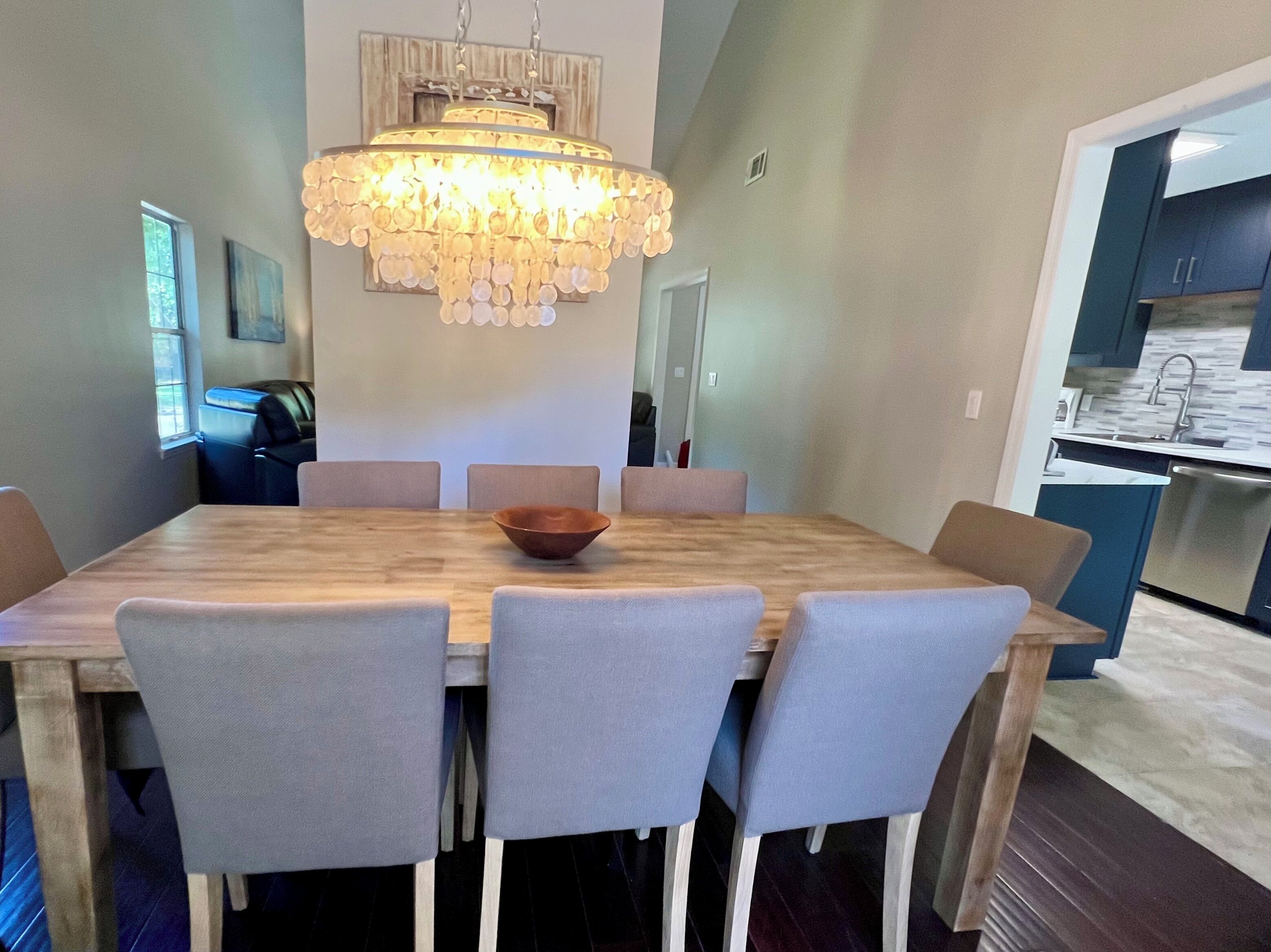 A dining area with a wooden table and six chairs, a chandelier, and a view into the kitchen.