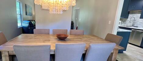 A dining area with a wooden table and six chairs, a chandelier, and a view into the kitchen.