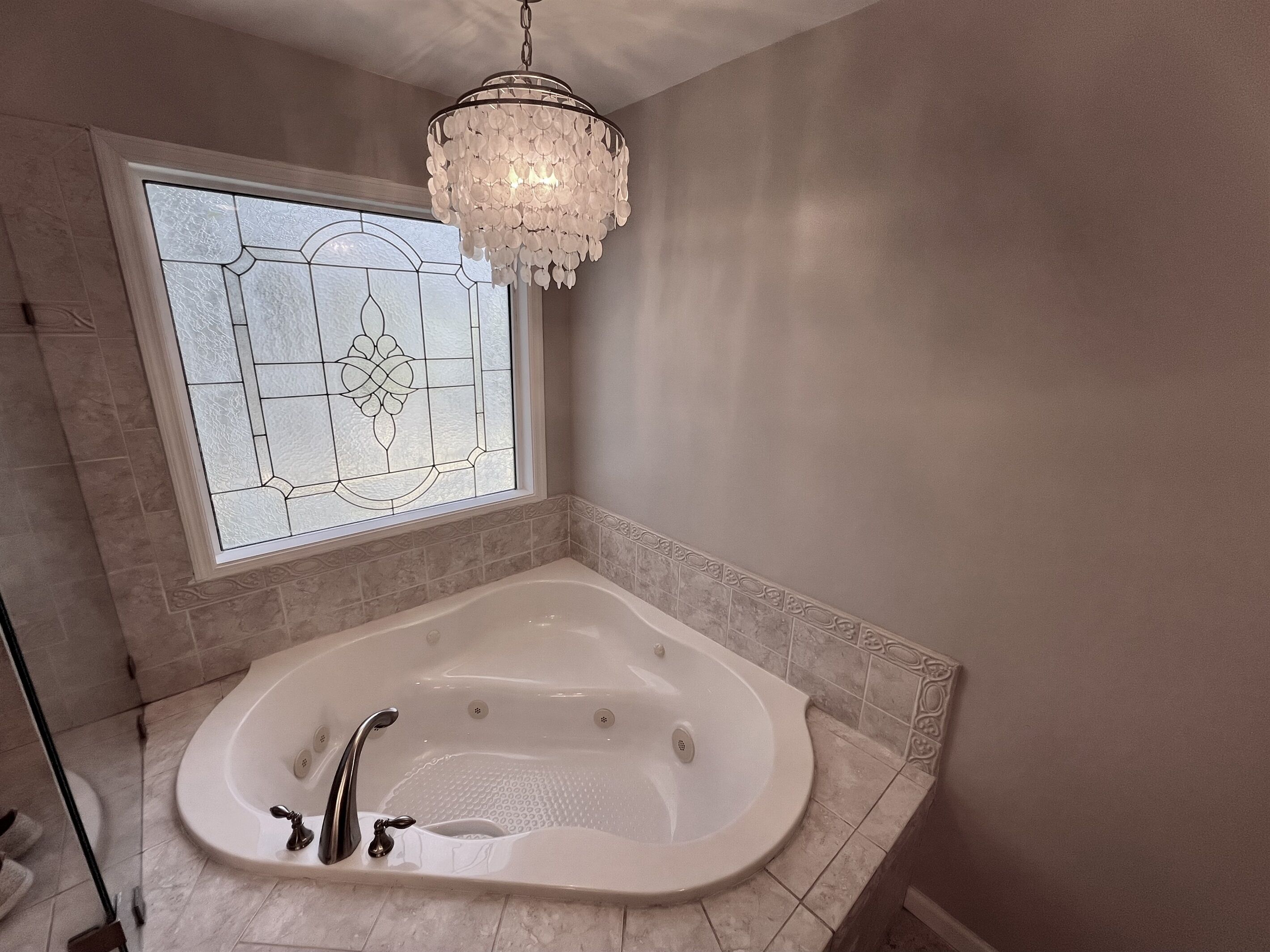 A bathroom with a freestanding bathtub, a large window with stained glass, and a chandelier.