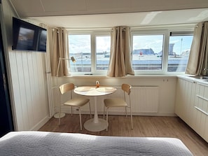 Une pièce comprenant un lit, une table avec des chaises, un téléviseur fixé au mur et des fenêtres avec des rideaux.