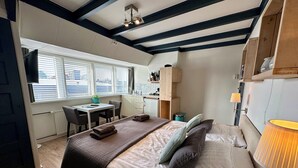 A compact bedroom with a bed, bedside table, lamp, and a view of the city through the window. - Nice studio with small terrace and parking lot. Only 200 meters from the sandy beach (Bergen aan Zee)
