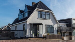 A modern two-story house with a white exterior, black roof, and large windows. - Nice studio with small terrace and parking lot. Only 200 meters from the sandy beach (Bergen aan Zee)