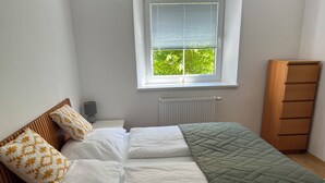 A bedroom with a bed, a window with blinds, a radiator, and a wooden wardrobe.