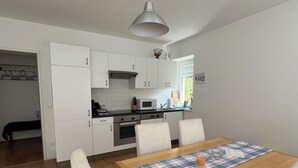 A compact kitchen with white cabinets, a wooden dining table, and a plaid placemat.