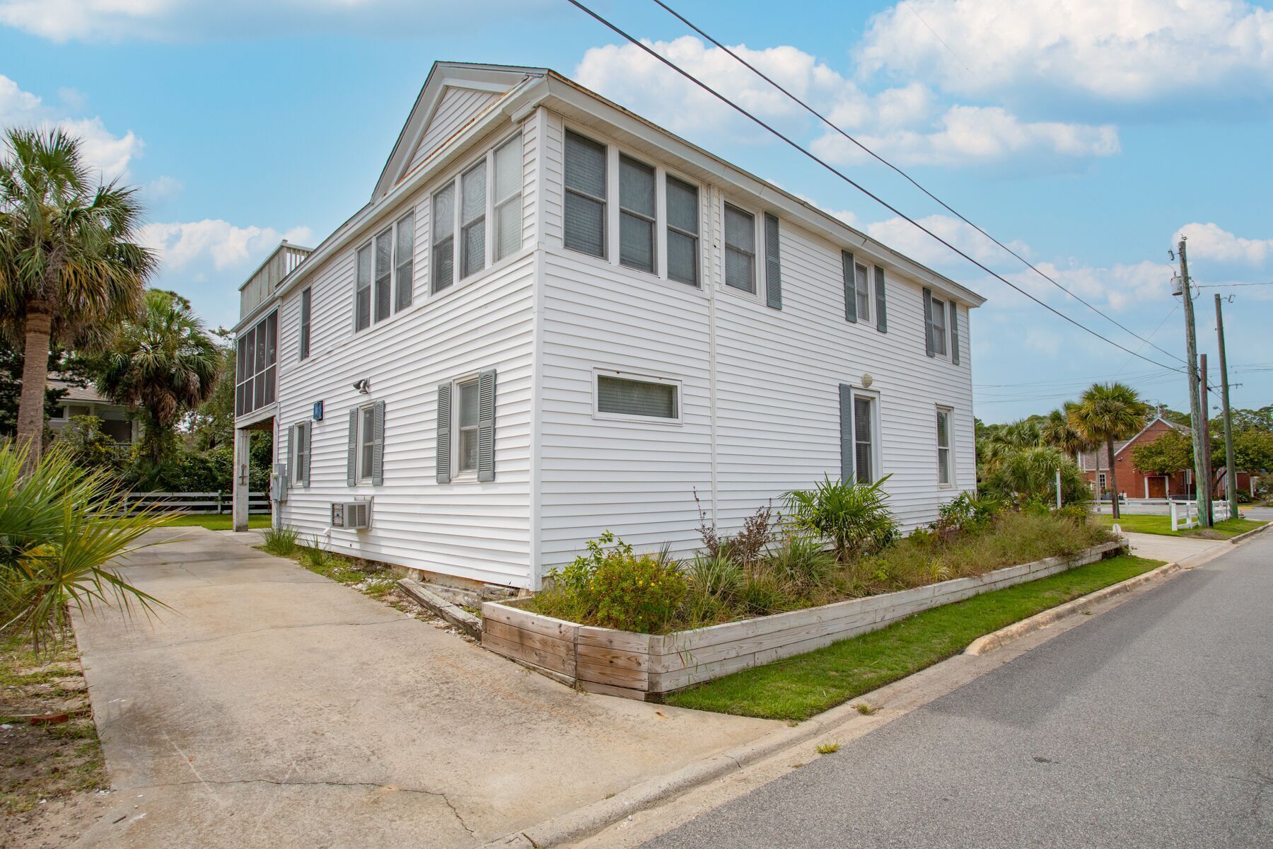 A white two-story house with a front porch, a small garden, and a street view.