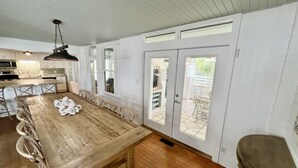 Eine geräumige Küche mit einem langen Holztisch, weißen Schränken und Blick ins Freie.