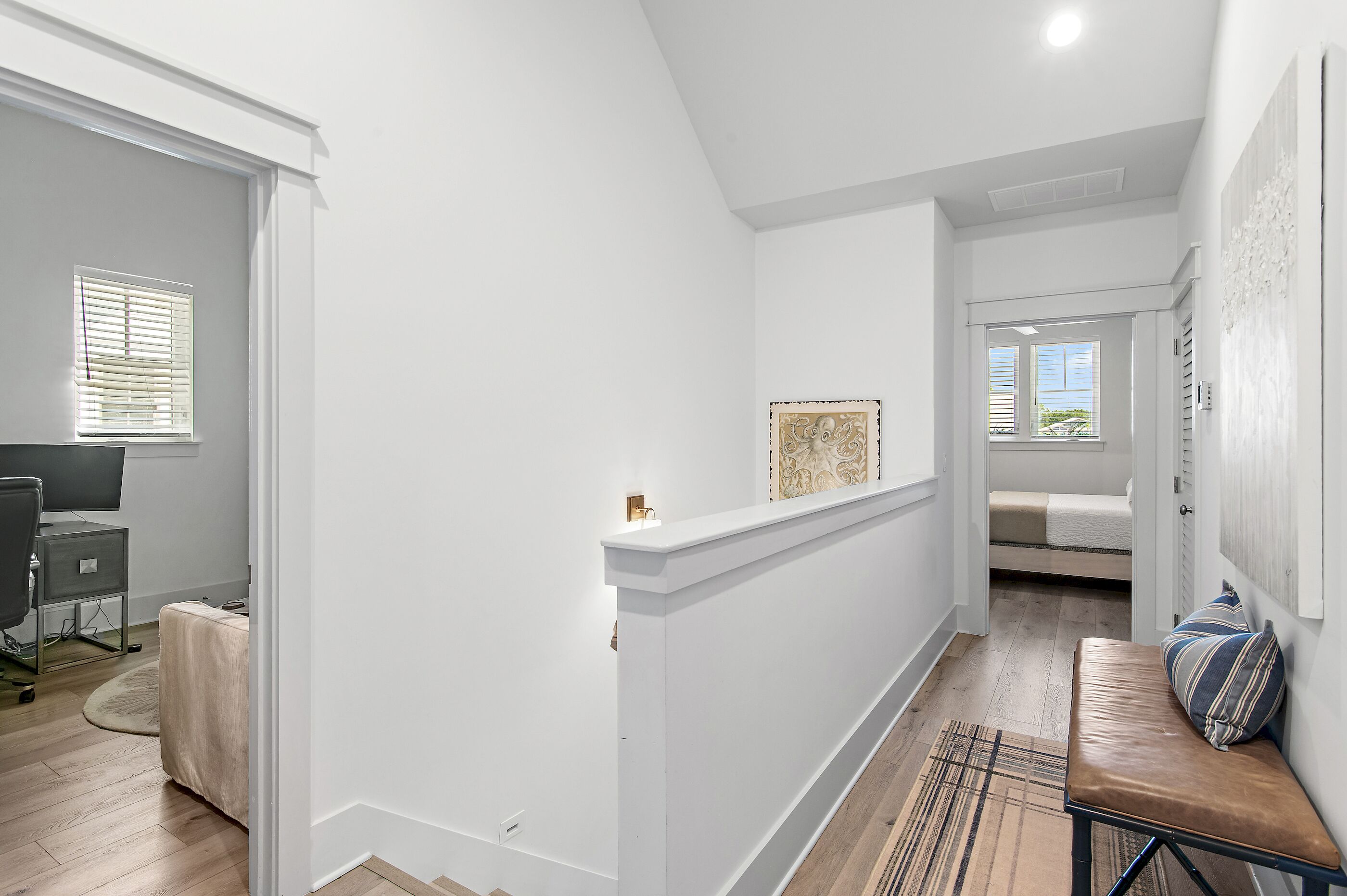 A hallway with a bench, a desk, and a bed in the background.