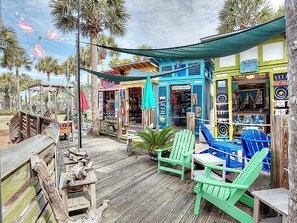 A wooden deck with green Adirondack chairs, a small table, and a tiki bar with colorful decorations. - ☀️Beach Access-3 Pools-Gulf View-Gulf Place Cabanas 210 (Santa Rosa Beach)