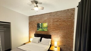 A hotel room with a brick wall, a bed with white linens, a ceiling fan, and two bedside lamps. - Stylish Historic Loft in Downtown Dubuque. Walk to Dining & Riverwalk (Dubuque)