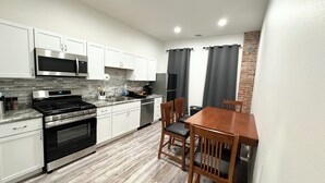 A modern kitchen with white cabinets, stainless steel appliances, and a wooden dining table. - Stylish Historic Loft in Downtown Dubuque. Walk to Dining & Riverwalk (Dubuque)