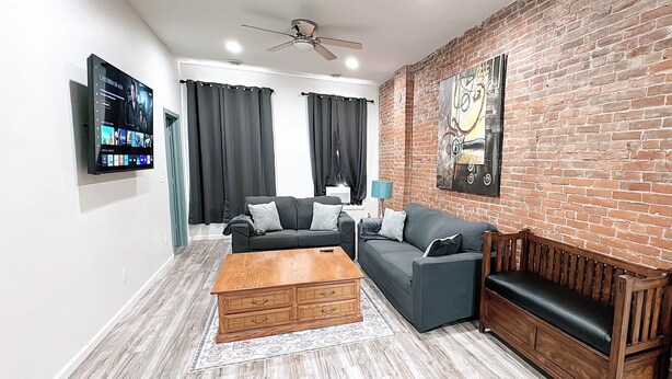 A living room with a brick wall, two sofas, a wooden coffee table, and a ceiling fan. - Stylish Historic Loft in Downtown Dubuque. Walk to Dining & Riverwalk (Dubuque)