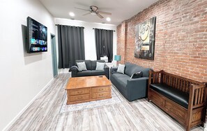 A living room with a brick wall, two sofas, a wooden coffee table, and a ceiling fan.