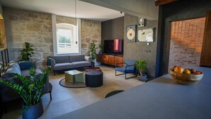Un salon moderne avec un mur en pierre, un grand téléviseur et un coin repas agrémenté d’un saladier de fruits.