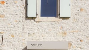 Un bâtiment avec une façade en pierre, une porte moderne portant l’inscription « sarizol » et des plantes en pot.