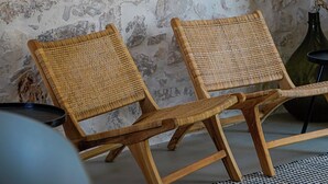 Une pièce avec un mur en pierre, deux fauteuils en osier et une étagère où sont exposées des œuvres d’art encadrées.