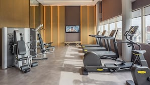 Uma academia moderna com equipamentos de cardio, máquinas de peso e uma tela de televisão.