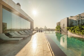 Un espace piscine aménagé sur le toit, avec des chaises longues et une vue dégagée sur les bâtiments de la ville.