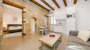 Una sala de estar moderna con un arco de piedra, un sofá, una mesa de centro y una cocina con armarios blancos y un microondas.
