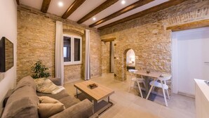 Una sala de estar acogedora con pared de piedra, vigas de madera, un sofá, una mesa de centro y un comedor con sillas.