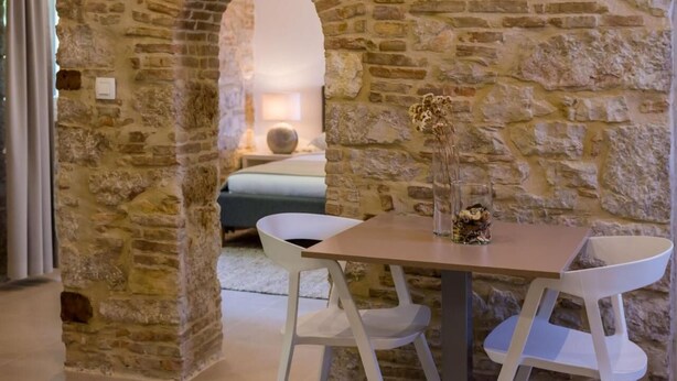 Una habitación con paredes de piedra, una mesa y dos sillas blancas.