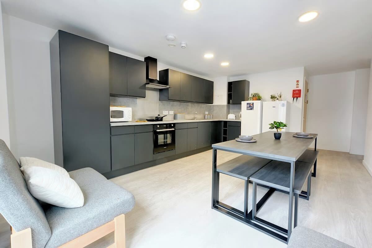 Uma cozinha moderna com armários escuros, forno embutido e área de refeições com mesa e banco.