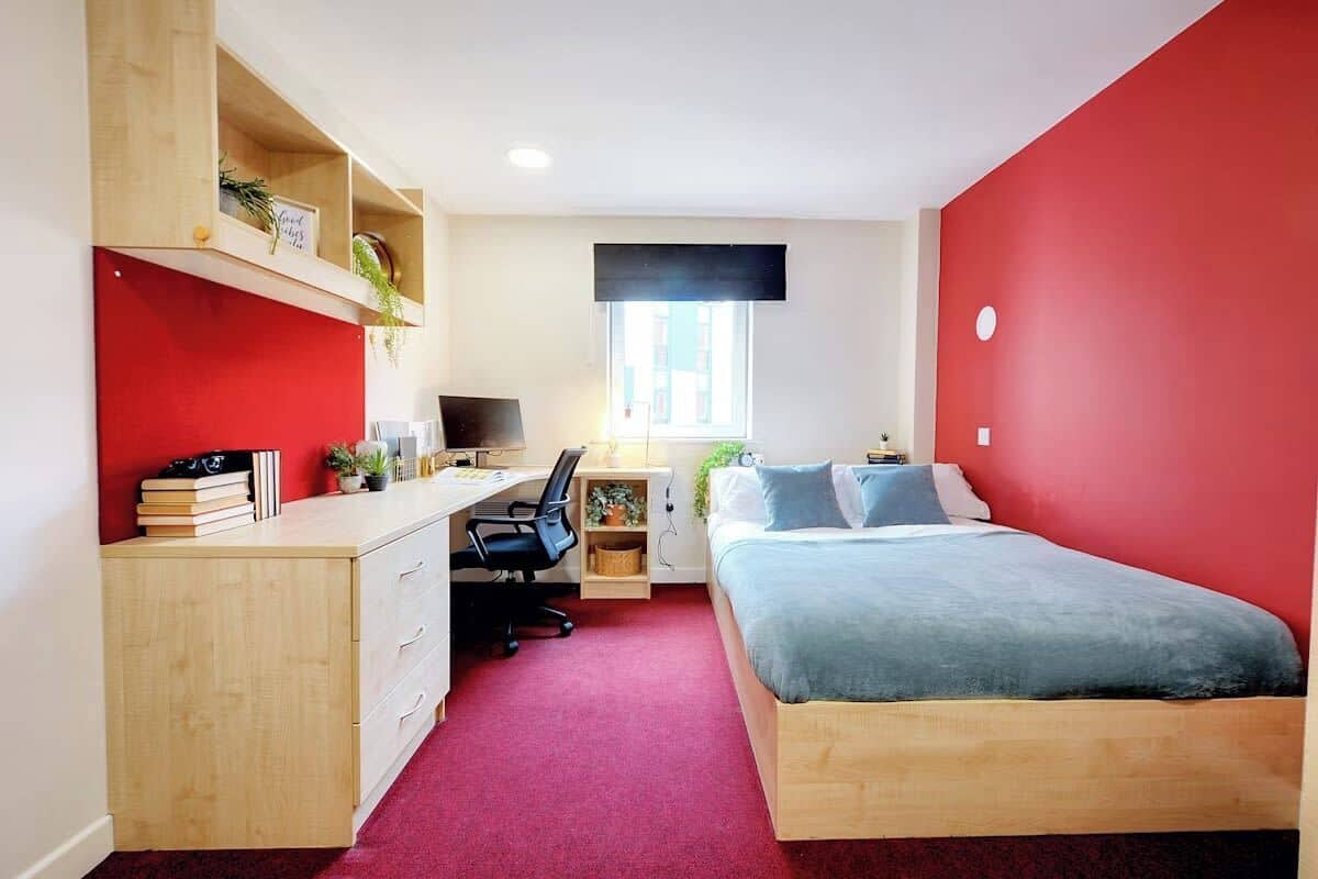 A bedroom with a bed, desk, chair, and shelving unit.