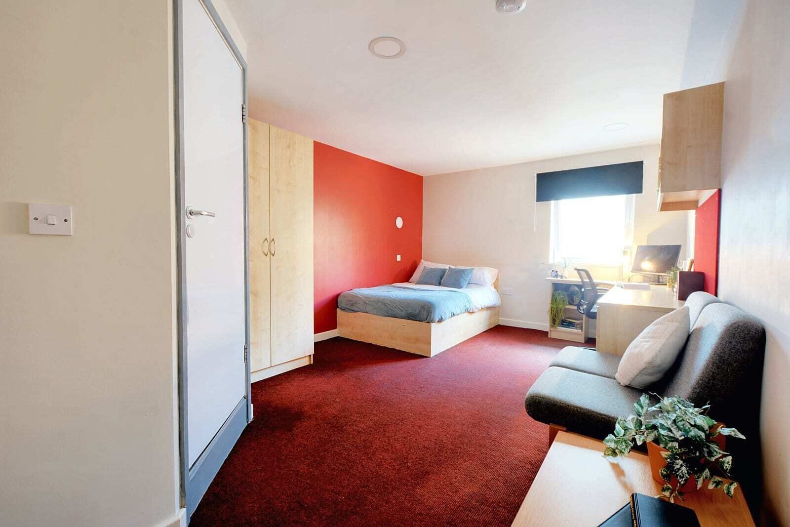 A compact bedroom with a bed, a desk, and a sofa.