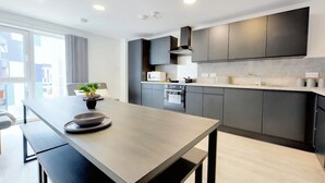A modern kitchen with dark cabinetry, a central island, and a view of the city. - For Students Only Nottingham Two (Nottingham)