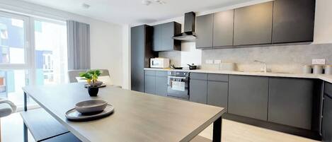 A modern kitchen with dark cabinets, a central island, and a large window.