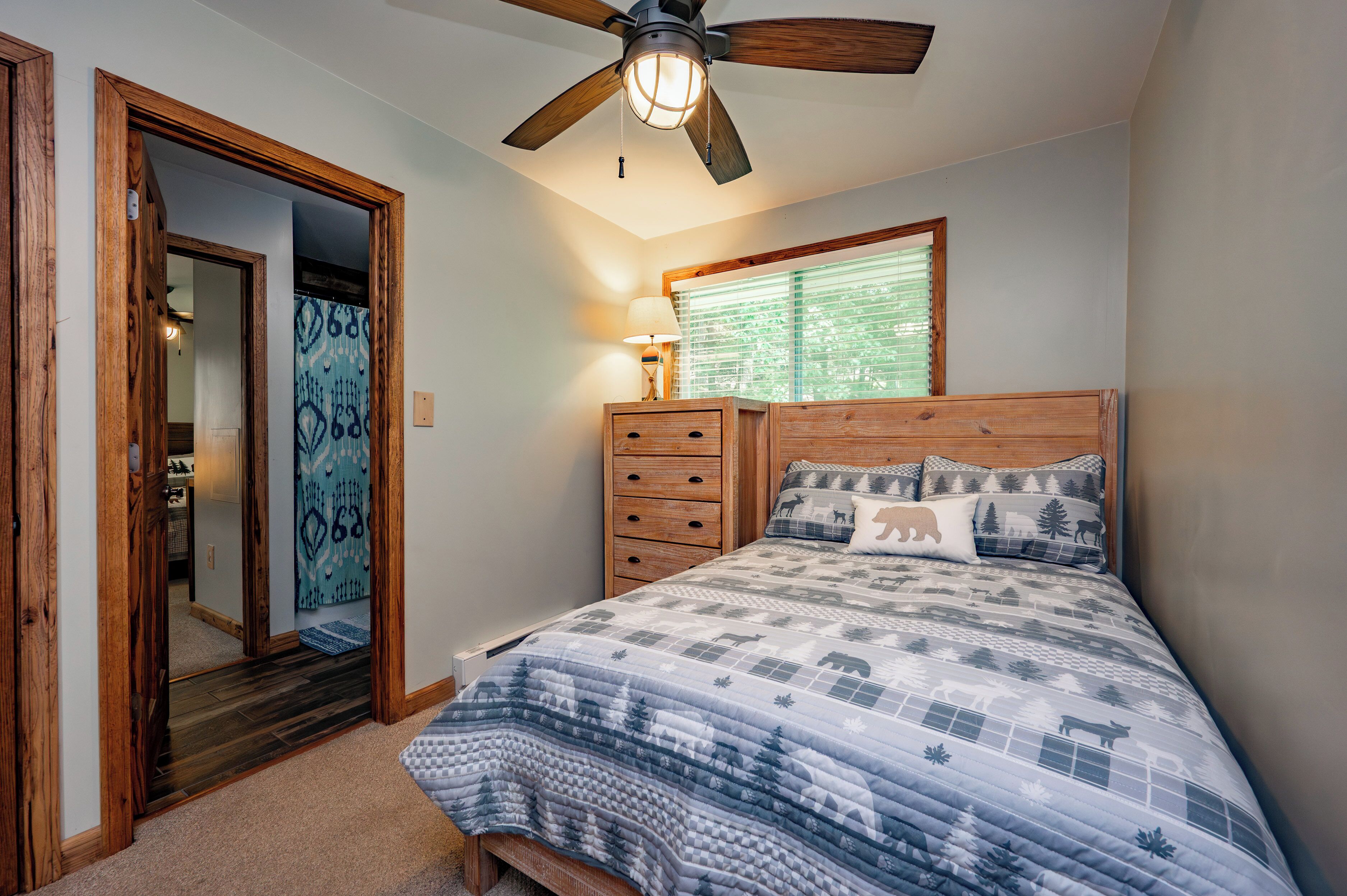 A bedroom with a wooden headboard, a bed with a quilted blanket, a ceiling fan, a window with blinds, and a wooden dresser.