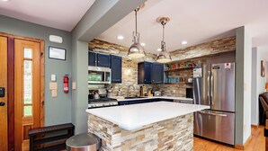 A modern kitchen with a large island, stainless steel appliances, and a stone backsplash. - Deep Creek Escape: w/ Theater, Fire Pit & Dock (Swanton)