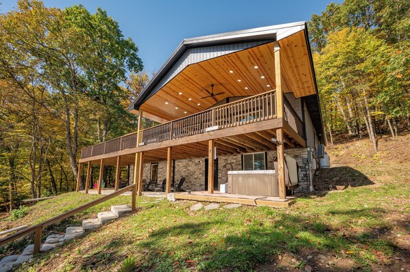 A two-story wooden cabin with a balcony, stone walls, and a hot tub.