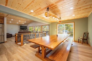A spacious kitchen with a built-in oven, a dining area with a long wooden table, and a view of the outdoors through large windows.