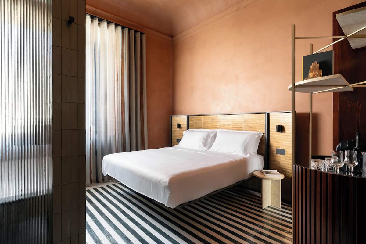 A hotel room with a large bed, a bedside table, a small round table, and a decorative shelf with glasses.