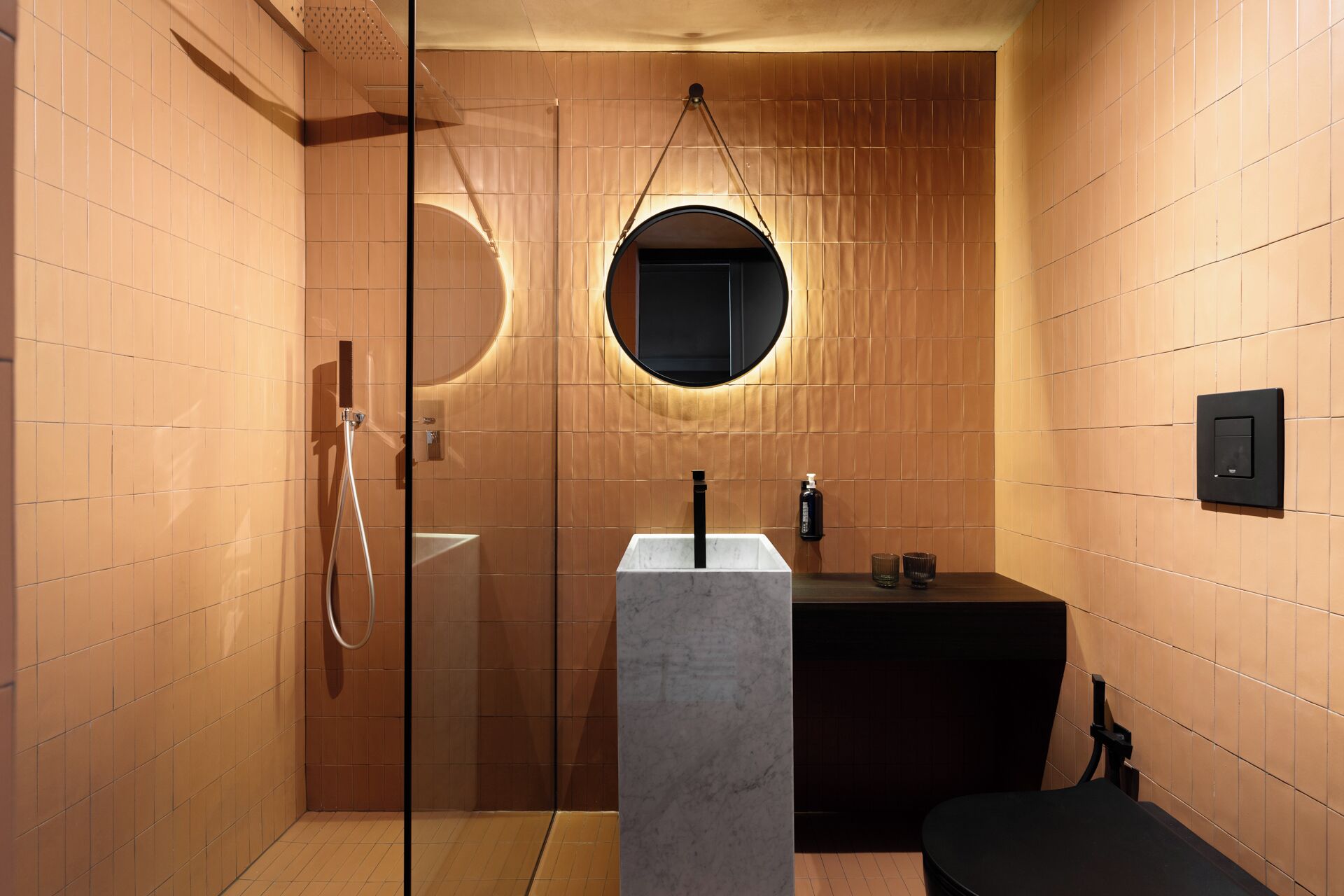 A modern bathroom with a glass-enclosed shower, a round mirror, and a marble sink.