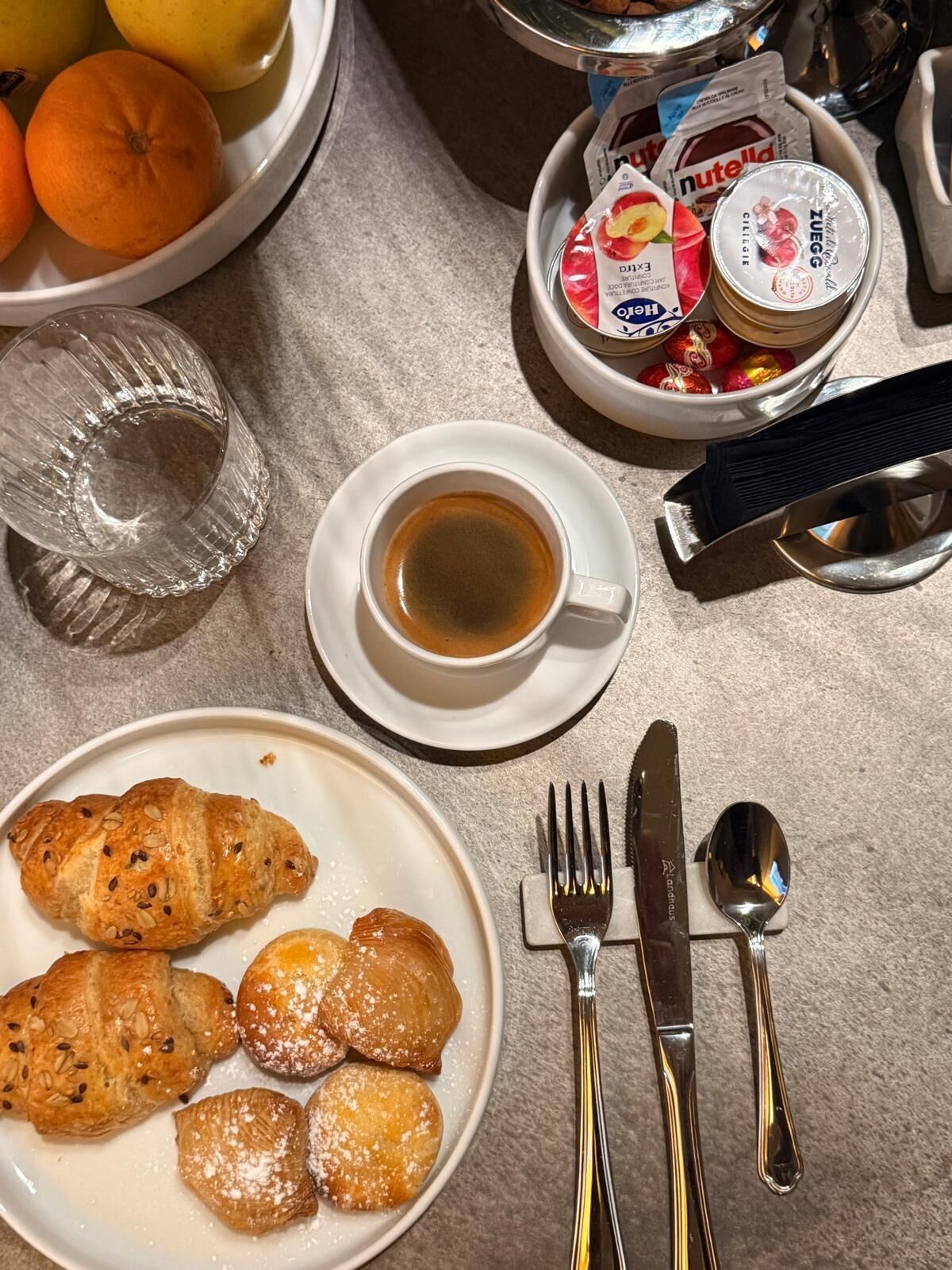 A breakfast setting with croissants, a cup of coffee, and a plate of fruit.