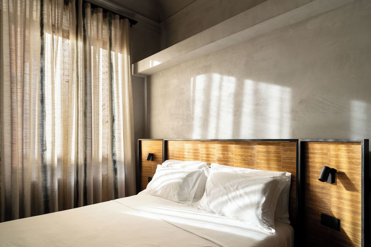 A modern hotel room with a large bed, wooden headboard, and a view of the city skyline.