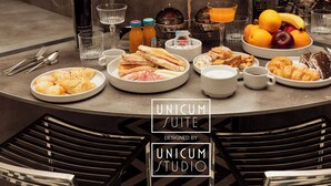 A round dining table with plates of food, glasses, and a potted plant in the background. - Unicum Suite Grande Archivio Napoli  (Naples)