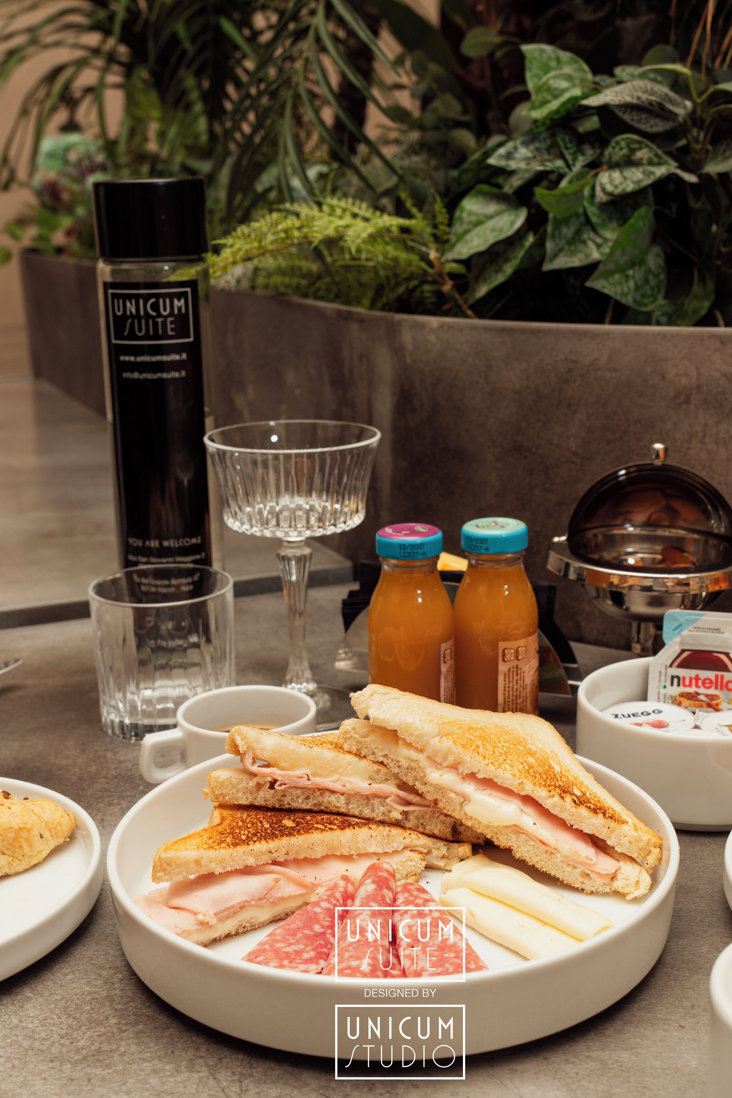 Ein Frühstück mit einem Sandwich, einer Saftflasche, einem Glas und einer Wasserflasche.