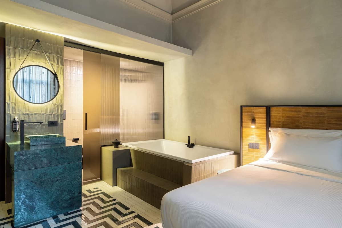 A hotel room with a large bed, a bathroom with a bathtub, a sink, and a mirror.