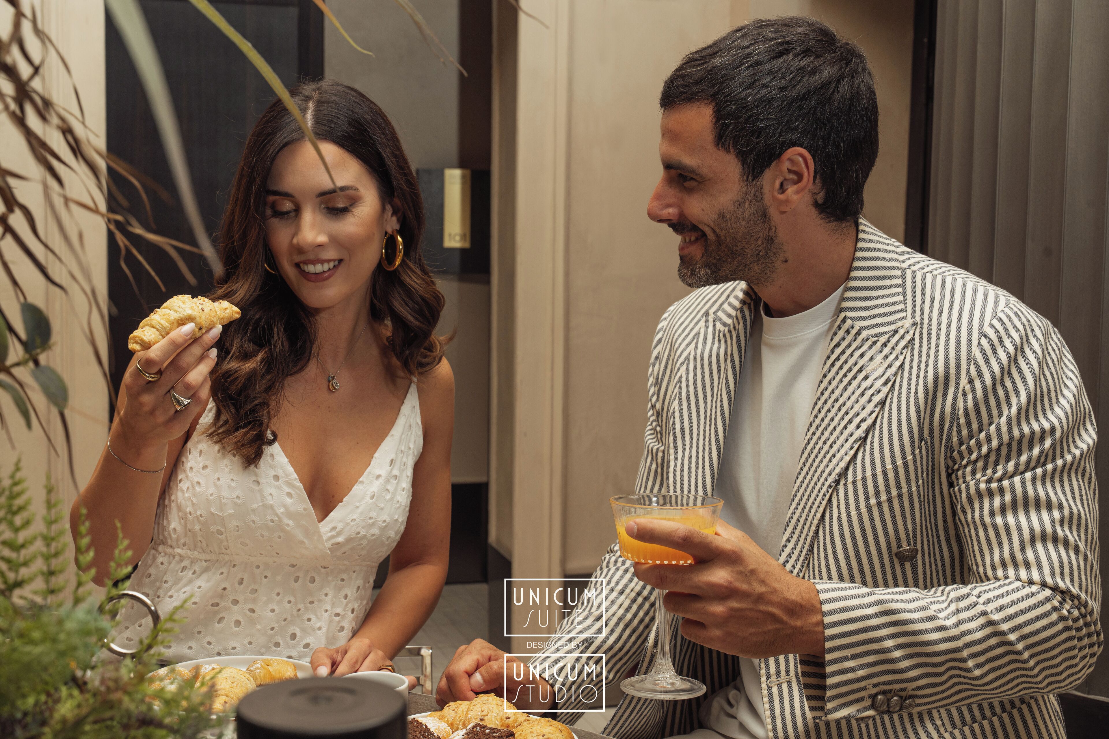Un couple est assis à une table, devant un verre de jus d’orange et une assiette de pâtisseries.