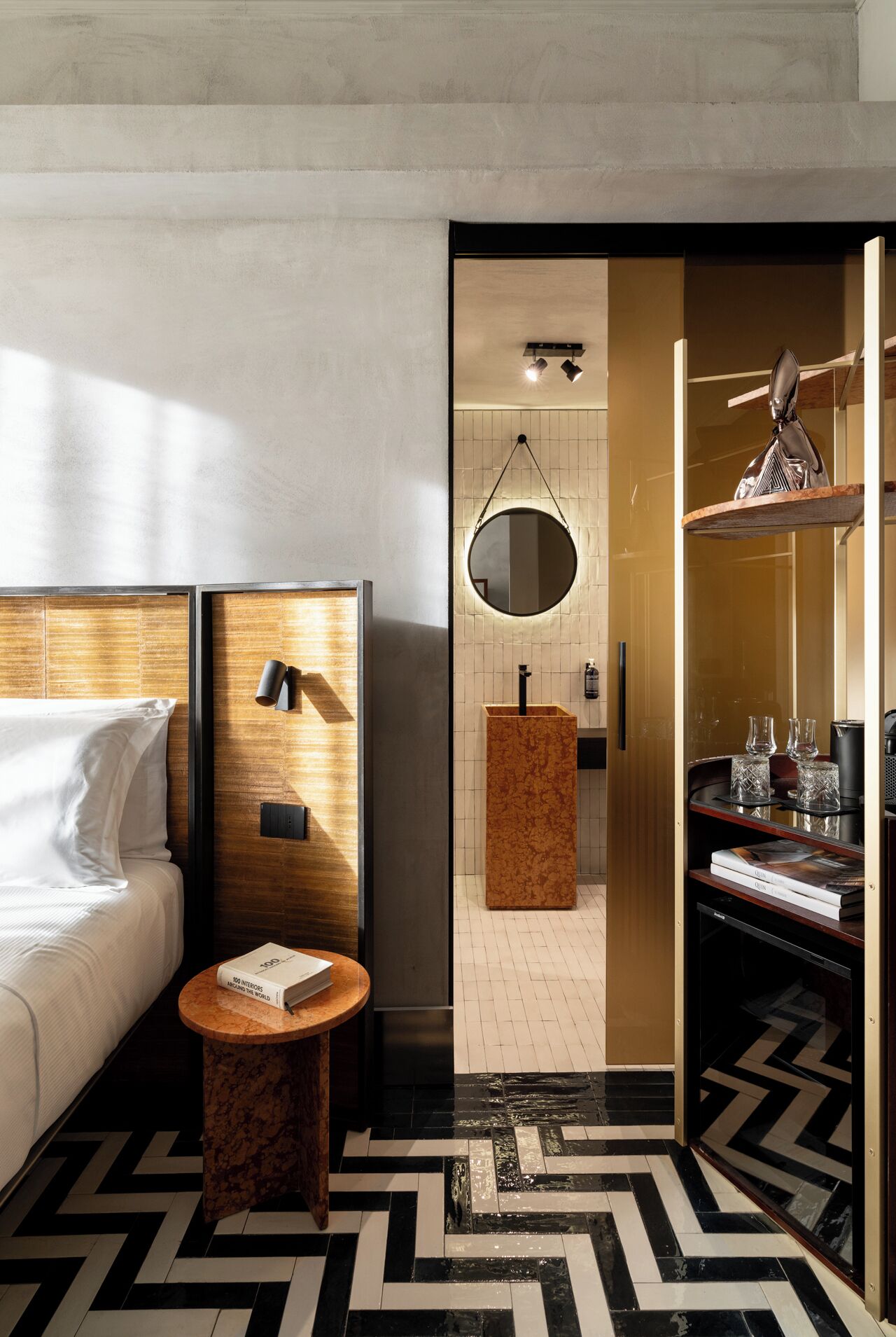 Une chambre d’hôtel moderne équipée d’un lit, d’un miroir rond, d’une table de chevet en bois et d’un mini-bar.