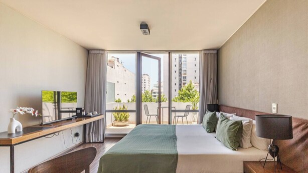 A hotel room with a bed, a desk with a TV, a balcony with a view of buildings and greenery. - Disfruta este Genial Dep en PalermoT707 (Buenos Aires)