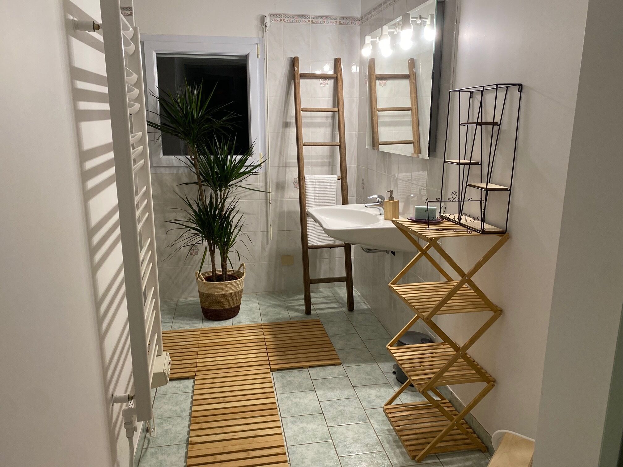 A bathroom with a wooden floor, a sink, a mirror, a potted plant, and a wooden ladder.