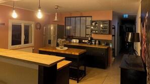 Une cuisine compacte dotée d’un îlot central, d’un réfrigérateur et d’un four à micro-ondes. Des luminaires suspendus sont placés au-dessus de l’îlot, et une fenêtre offre une vue agréable.