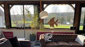 Un salon chaleureux avec un canapé en cuir marron, un fauteuil à motifs et une grande fenêtre donnant sur un paysage verdoyant.
